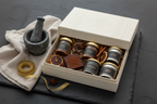 Gift box with small jars, a mortar and pestle, and spices on a dark surface